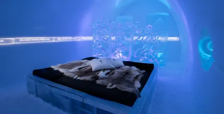 en säng med renskinn i ett vackert rum av is och snö på icehotel