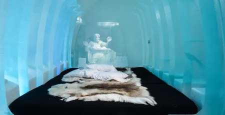 en säng med renskinn i ett vackert rum av is och snö på icehotel